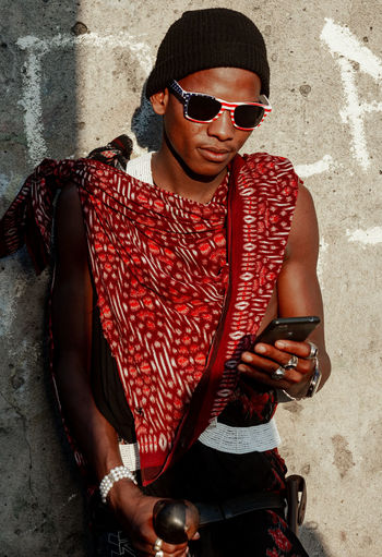 Young man wearing sunglasses using smart phone against wall