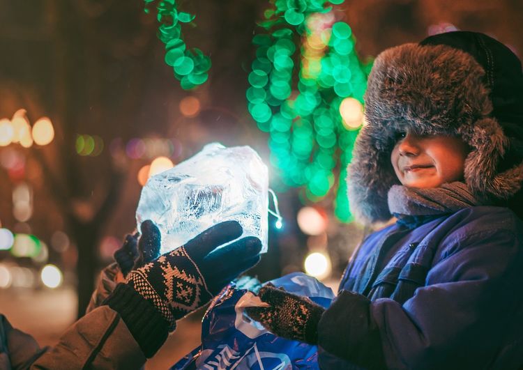 Portrait of smiling boy looking at ice chunk at night