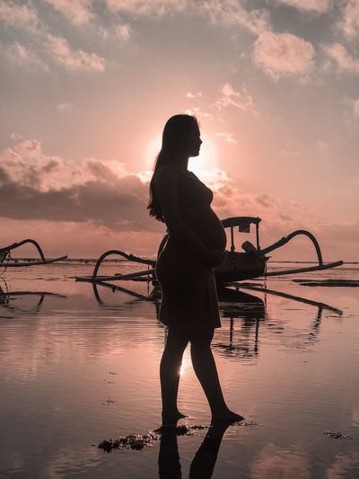 Silhouette pregnant woman standing by sea against sky during sunrise