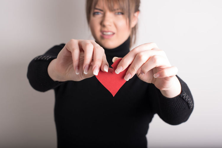 Portrait of woman tearing heart shape paper against wall