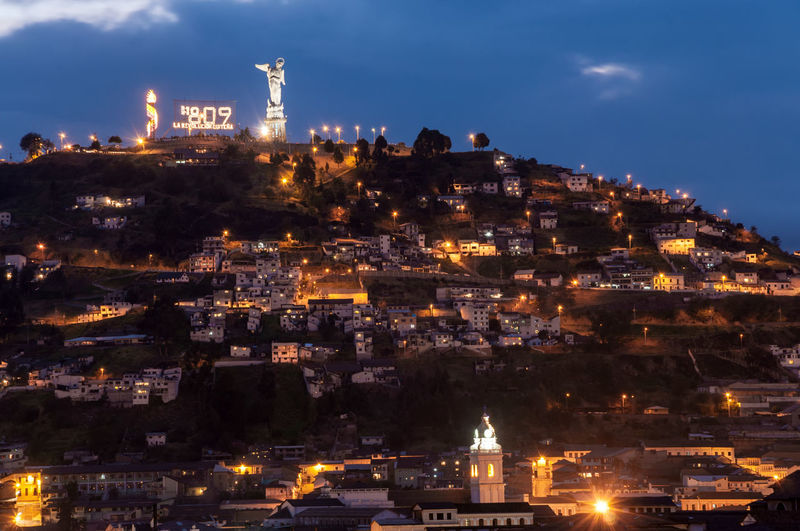 Low angle view of illuminated houses and virgin mary on el panecillo against sky