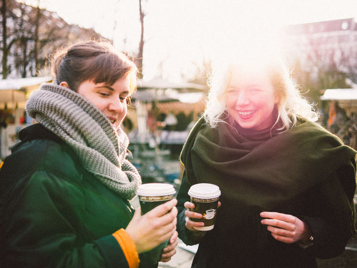 Happy friends holding disposable coffee cup in flea market