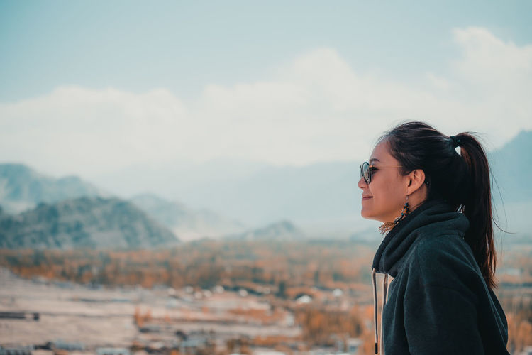 Side view of woman looking at mountains against sky