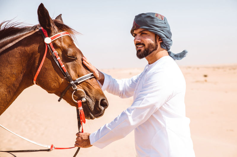 Man with horse in desert against sky