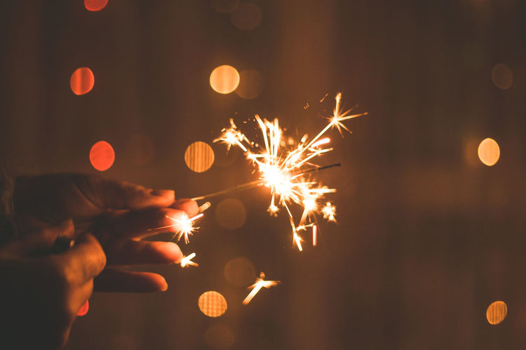 Cropped hands of woman holding lit sparkler at night