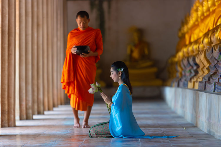 Side view of woman praying while monk walking in buddhist temple
