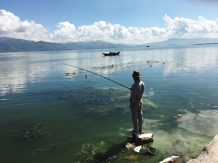 Rear view of man fishing in sea against sky