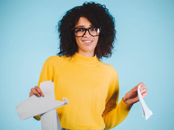 Portrait of young woman tearing papers against blue background