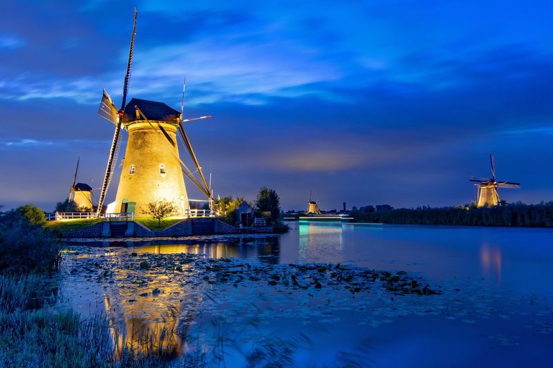 Traditional windmill by river against blue sky