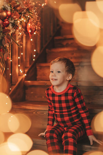 Portrait of cute girl sitting on illuminated christmas tree