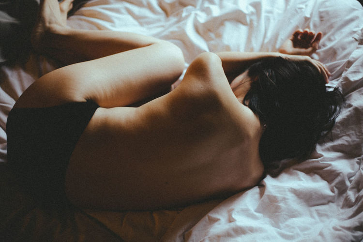 High angle view of shirtless woman lying on bed