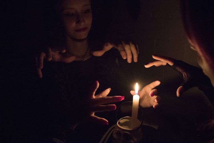 Women practicing witchcraft by burning candle in darkroom