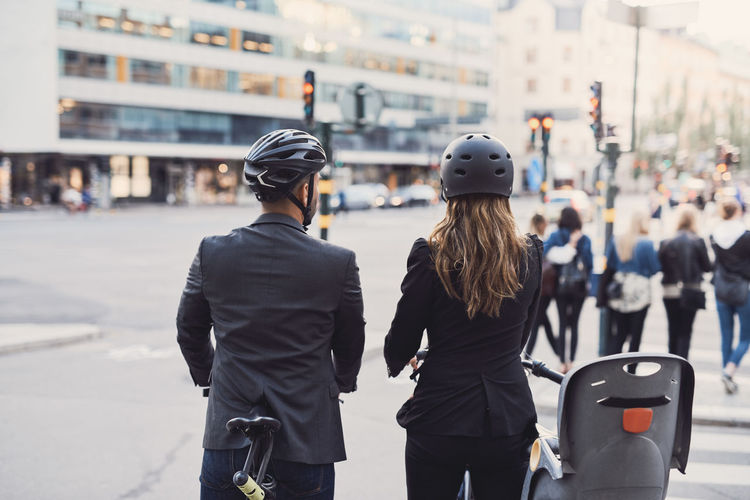 Rear view of business colleagues with bicycles on street in city