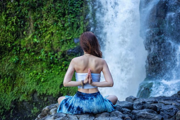 Rear view of woman practicing yoga while looking at waterfall