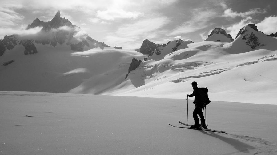Silhouette skier standing on snowcapped mountain against cloudy sky