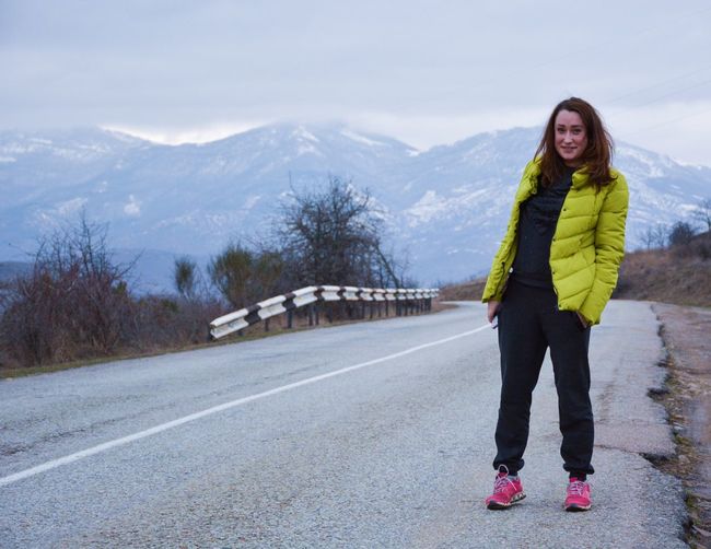 Full length portrait of woman standing on road against mountains during winter