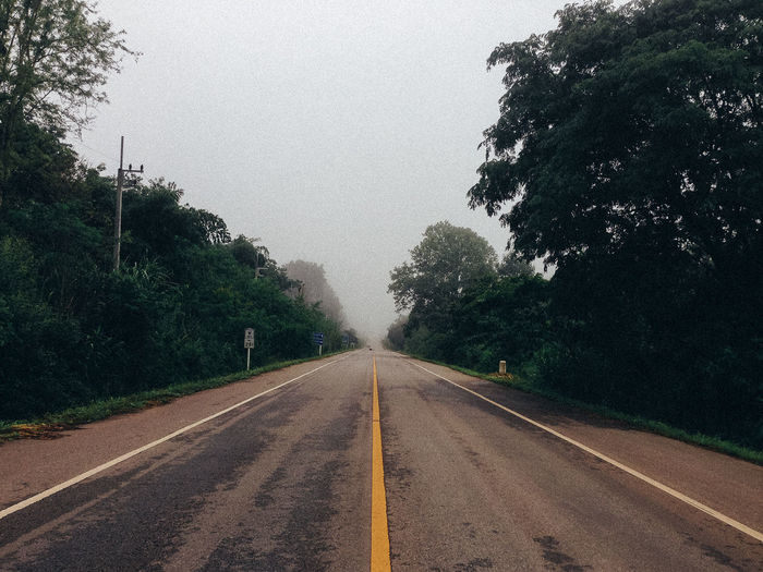 Empty road amidst trees against sky during rainy season