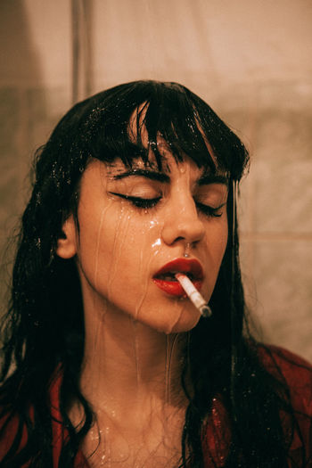 Close-up of wet woman smoking cigarette in bathroom