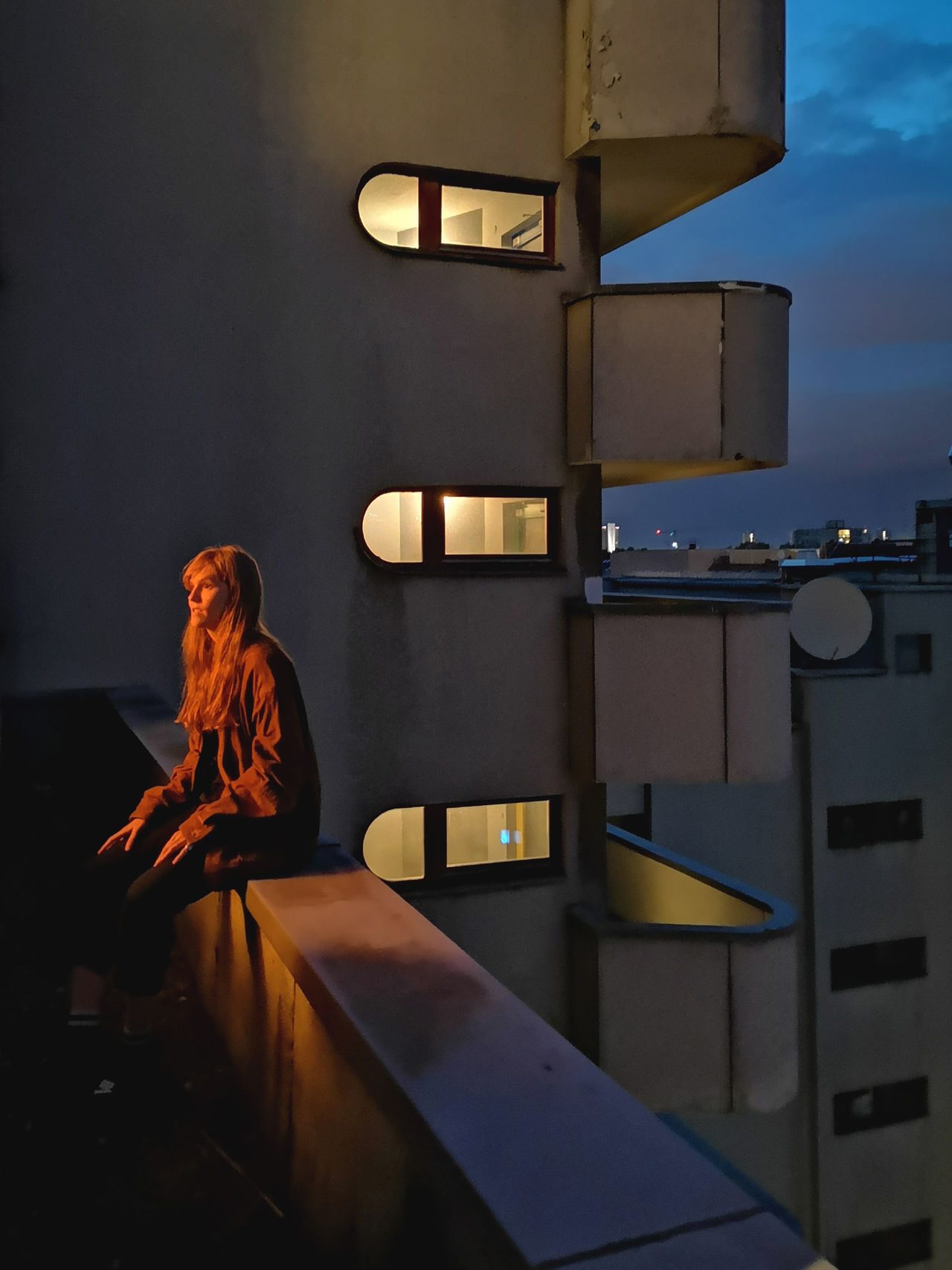 Woman sitting on retaining wall in balcony at night
