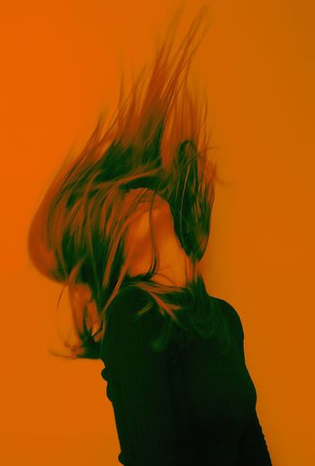 Blurred motion of woman with tousled hair against orange background
