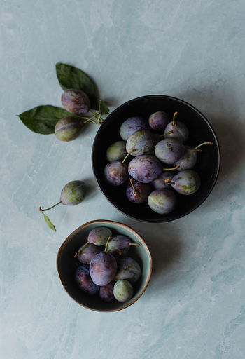 Overhead shot of bowls of fresh plums against a marble background.
