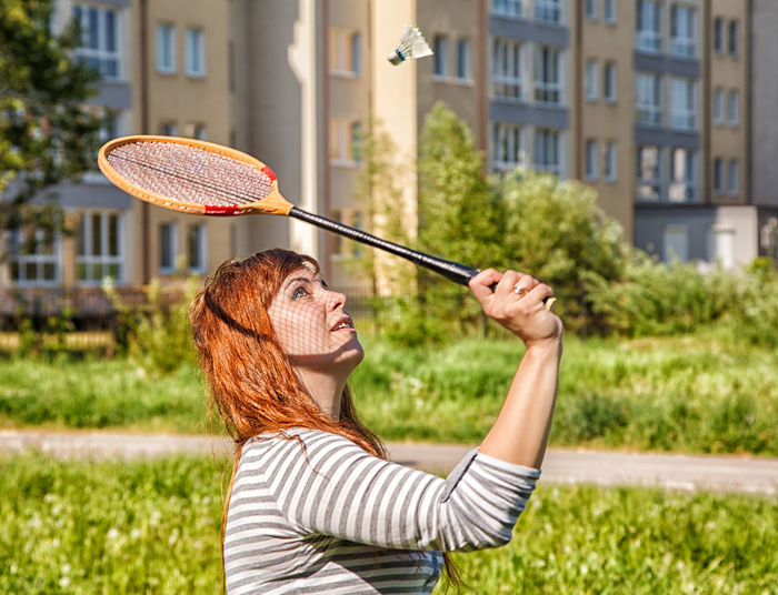 Side view of young woman playing badminton while standing outdoors
