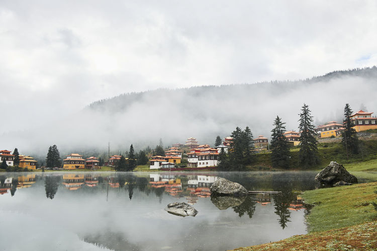 Scenery view of old buildings of tibetan buddhist temples located on shore of tranquil reflecting lake in highland covered with clouds