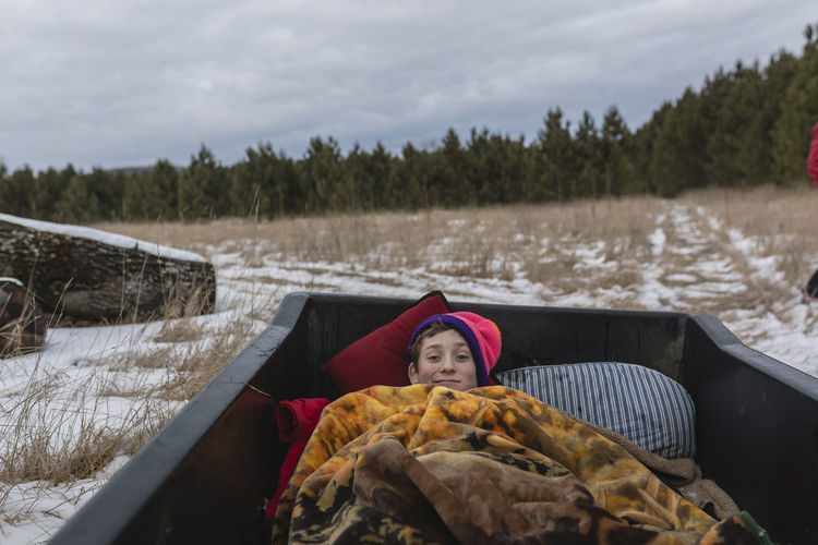 High angle portrait of teenage boy lying in off-road vehicle against sky during winter