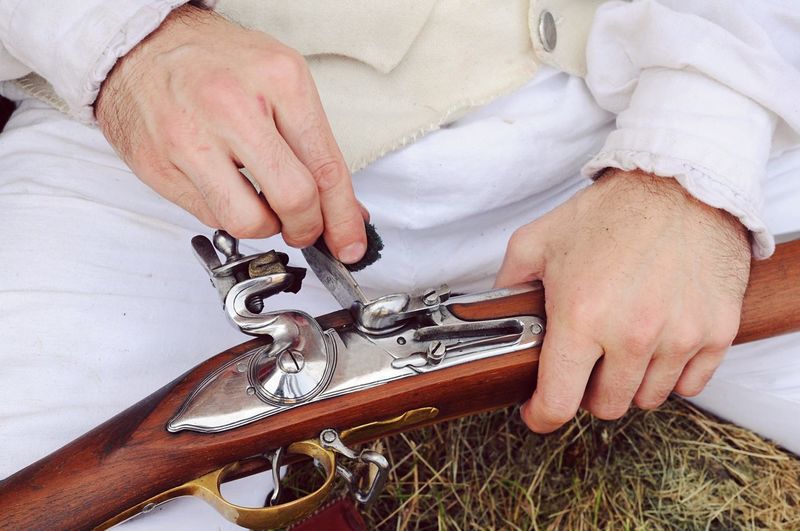 Cropped image of man cleaning gun at field