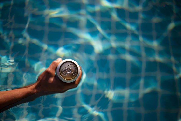 Selective focus white beer can in hand. man is soaking in the pool with an open beer