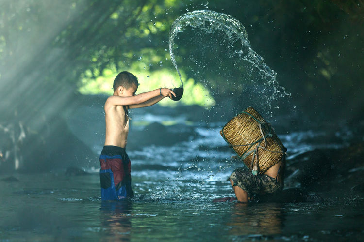 Side view of boy throwing water on man in basket at river