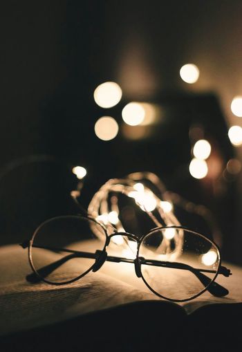 Close-up of eyeglasses against illuminated lights on book