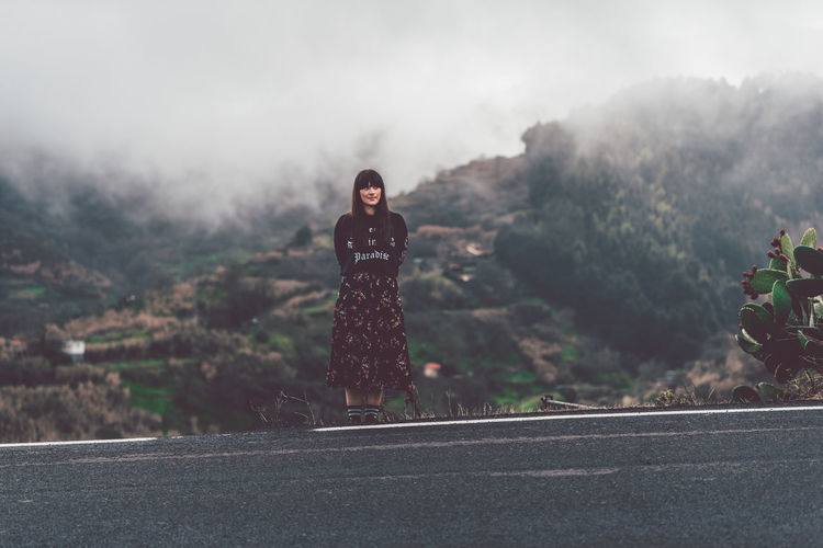 Young woman standing on road against mountain during foggy weather