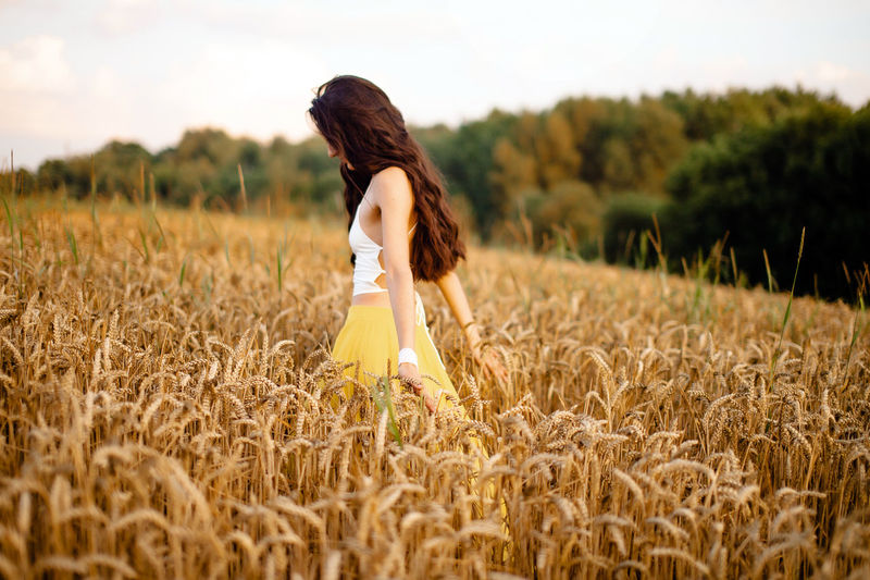 A girl runs through a field with spikelets against the background of the setting sun