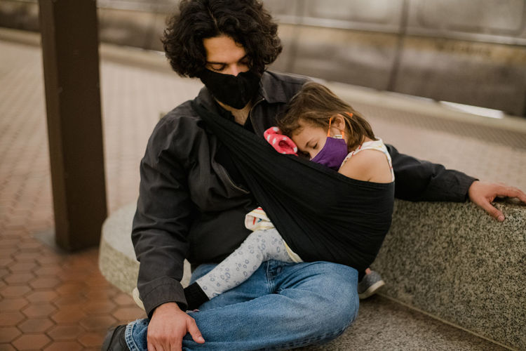Daughter sleeping in sling on dad wearing face masks