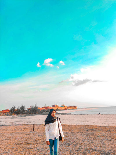 Young woman wearing hijab standing at beach against sky