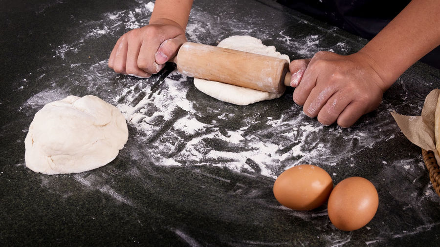 Cropped hands rolling dough on kitchen counter