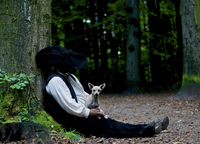 Hiker taking a break with his best friend, a dog under a tree in the forest