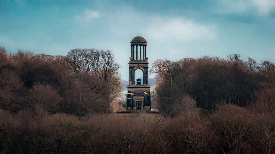 Old building by trees on field against sky