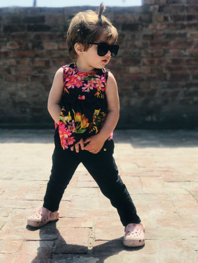 Girl wearing sunglasses standing against wall