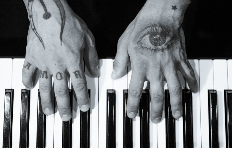Tattooed mans hands on the keyboard of a piano. dark background