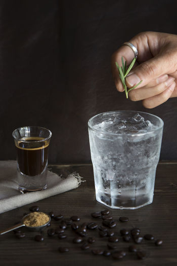 Cropped hand putting rosemary in clod drink on table