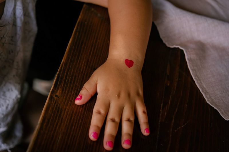 Midsection of girl's hand with red heart painted on it 