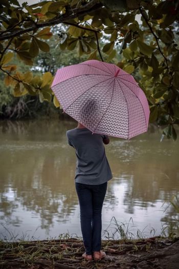 Rear view of girl holding umbrella while standing at lakeshore in forest