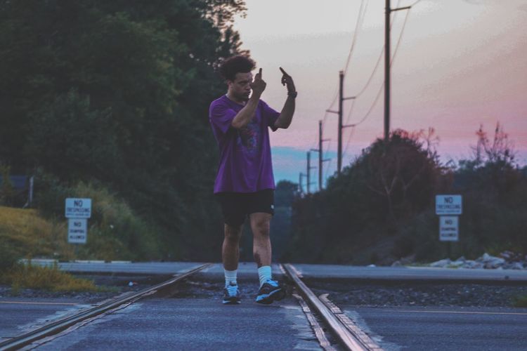Full length of man showing middle fingers while walking on railroad track during sunset