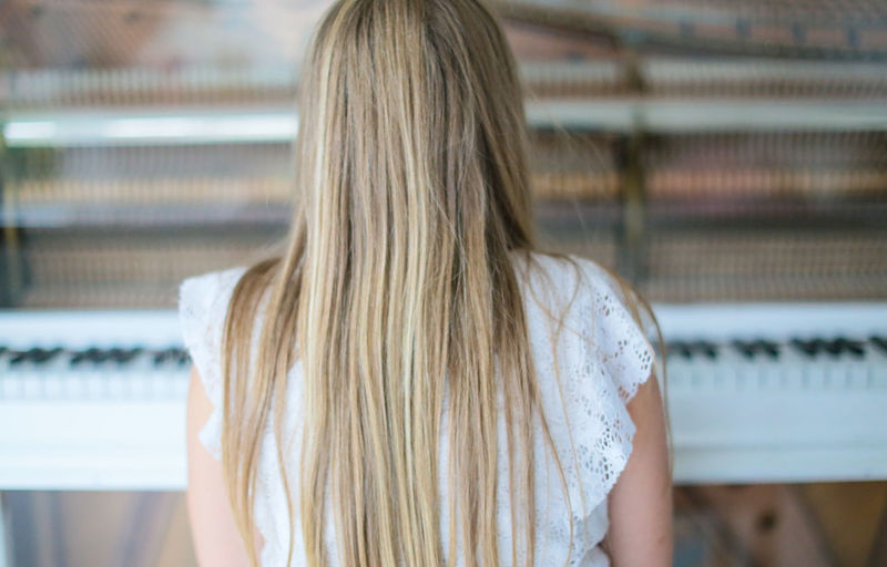 Rear view of blond woman sitting by grand piano at home