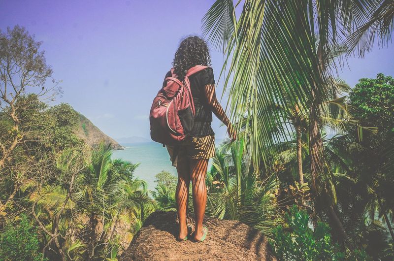 Rear view of young woman standing on rock against sky