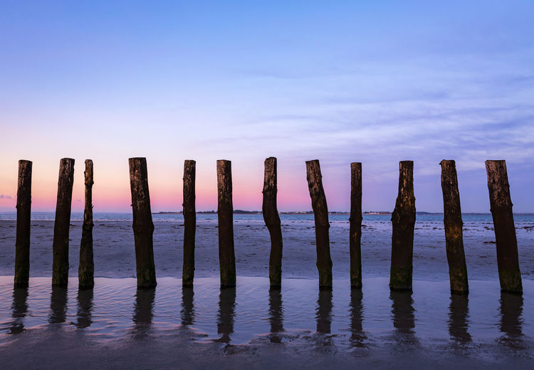 Wooden posts in sea against sky