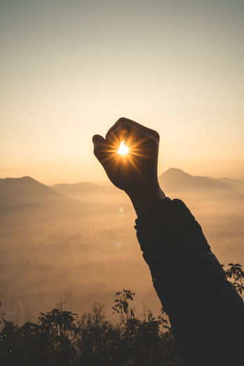 Cropped hand gesturing against sky during sunset