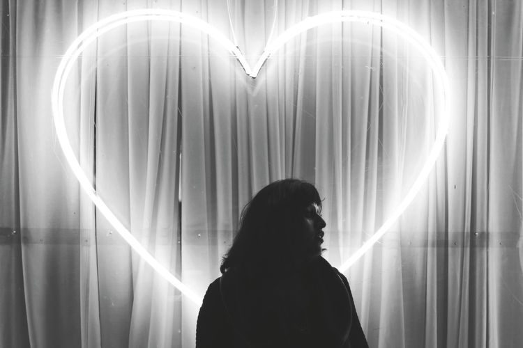 Woman standing in front of illuminated heart shape light painting